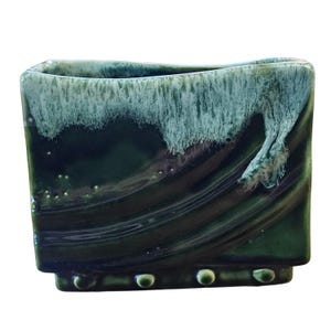 May include: A rectangular ceramic vase featuring a deep forest green glaze with a flowing, white drip pattern along the top rim. The base of the vase is accented with a row of small, raised circular beads, and the surface has a glossy finish.