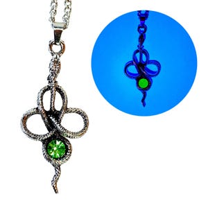 May include: Silver-toned snake pendant necklace with a green gemstone center. The pendant features a detailed snake design with a looped pattern and a dangling tail. The necklace is displayed on a white background.