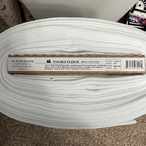 Pode incluir: Um rolo de tecido de lã polar fusível branco, com 114 cm de largura, para entretela, acolchoamento, acolchoado e artesanato. A etiqueta diz "FUSIBLE FLEECE" e "Made in the U.S.A."