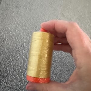 Peut inclure: Une bobine de fil doré avec une base et un dessus orange. Le fil est enveloppé dans du plastique transparent. Cette fourniture de couture est idéale pour divers projets de couture et d'artisanat.