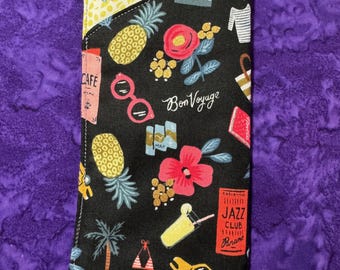 May include: A black passport holder with a colorful print of pineapples, flowers, sunglasses, palm trees, and a taxi. The text "Bon Voyage" is printed on the holder. The holder has a yellow and white lining.