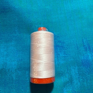 Könnte beinhalten: Eine weiße Garnrolle mit einer orangefarbenen Kunststoffspule. Die Rolle befindet sich auf einem blauen Hintergrund.