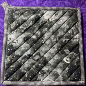 May include: A black and white quilted hot pad with a starry night design. The hot pad has a white border with a small checkered pattern.