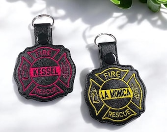 May include: Two black leather keychains with embroidered fire department logos. The first keychain has a red "FIRE" and "RESCUE" with the name "KESSEL" in the center. The second keychain has a yellow "FIRE" and "RESCUE" with the name "LA MONICA" in the center.