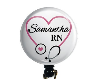 May include: A white retractable badge holder with a round button featuring a pink heart with a stethoscope inside. The button has the text "Samantha RN" in black.