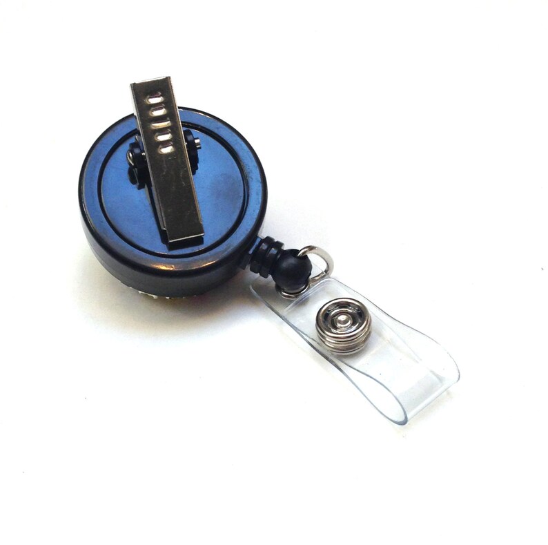 Peut inclure: Porte-badge r&eacute;tractable noir avec un clip argent&eacute; et une sangle en plastique transparente. La bobine a un bouton noir sur la sangle.
