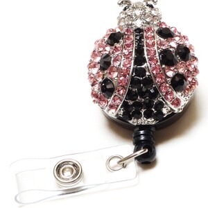 Peut inclure: Un porte-badge avec une breloque en forme de coccinelle orn&eacute;e de strass noirs et roses, une sangle en plastique transparente et un clip en m&eacute;tal argent&eacute;.