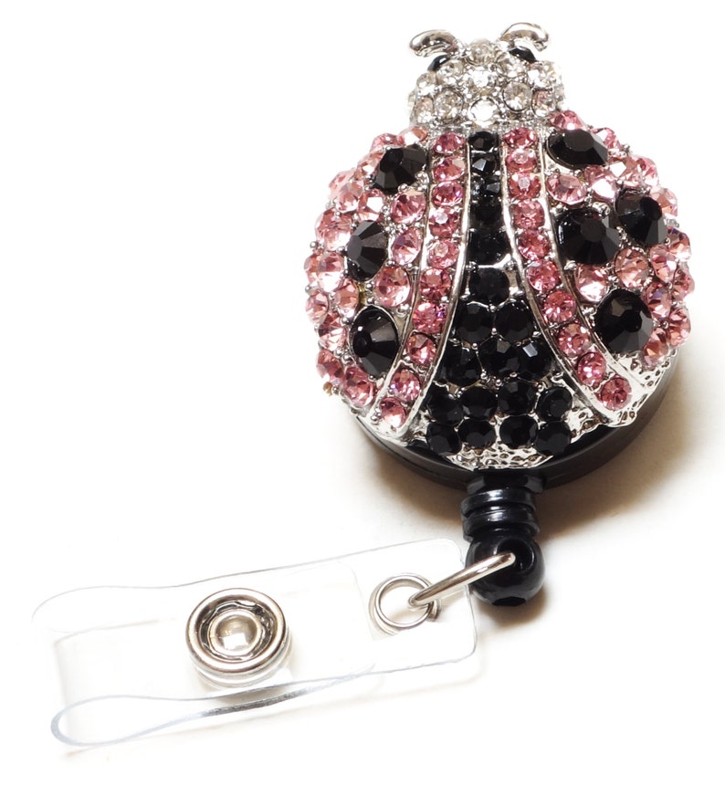 Peut inclure: Un porte-badge avec une breloque en forme de coccinelle orn&eacute;e de strass noirs et roses, une sangle en plastique transparente et un clip en m&eacute;tal argent&eacute;.