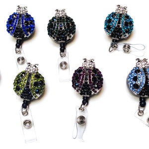 Peut inclure: Assortiment de huit porte-badges r&eacute;tractables en forme de coccinelle orn&eacute;s de strass de diff&eacute;rentes couleurs. Chaque porte-badges pr&eacute;sente une coccinelle de couleur diff&eacute;rente avec des accents noirs et un cordon r&eacute;tractable en plastique transparent.