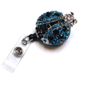 Peut inclure: Un porte-badge r&eacute;tractable argent&eacute; avec une sangle noire et un charme de coccinelle en strass bleu et noir.