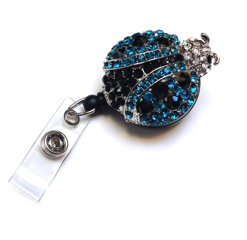 Peut inclure: Un porte-badge r&eacute;tractable argent&eacute; avec une sangle noire et un charme de coccinelle en strass bleu et noir.