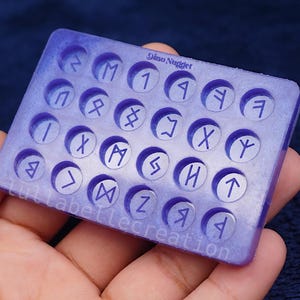 May include: A rectangular, lavender-colored resin mold with circular indentations, each containing a different rune symbol. The text "Dino Nugget" and "lullabellecreation" are visible on the mold.
