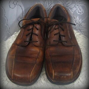 May include: A pair of brown leather lace-up shoes with a distressed look. The shoes have a rounded toe and a thick sole.