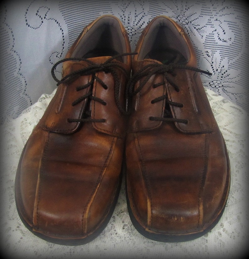 May include: A pair of brown leather lace-up shoes with a distressed look. The shoes have a rounded toe and a thick sole.