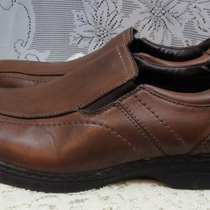 Puede incluir: Un par de zapatos marrones de cuero sin cordones con un dise&ntilde;o cosido y una suela de goma gruesa.