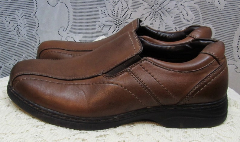 Puede incluir: Un par de zapatos marrones de cuero sin cordones con un dise&ntilde;o cosido y una suela de goma gruesa.