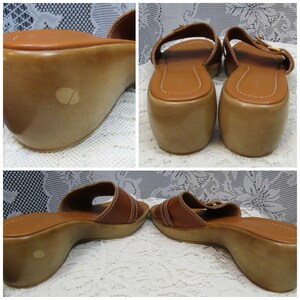 May include: A pair of brown leather wedge sandals with two straps and a buckle closure. The sandals have a wooden wedge heel.