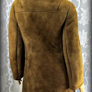 May include: A brown suede coat with a shearling collar. The coat has a long, fitted silhouette and a single-breasted closure.
