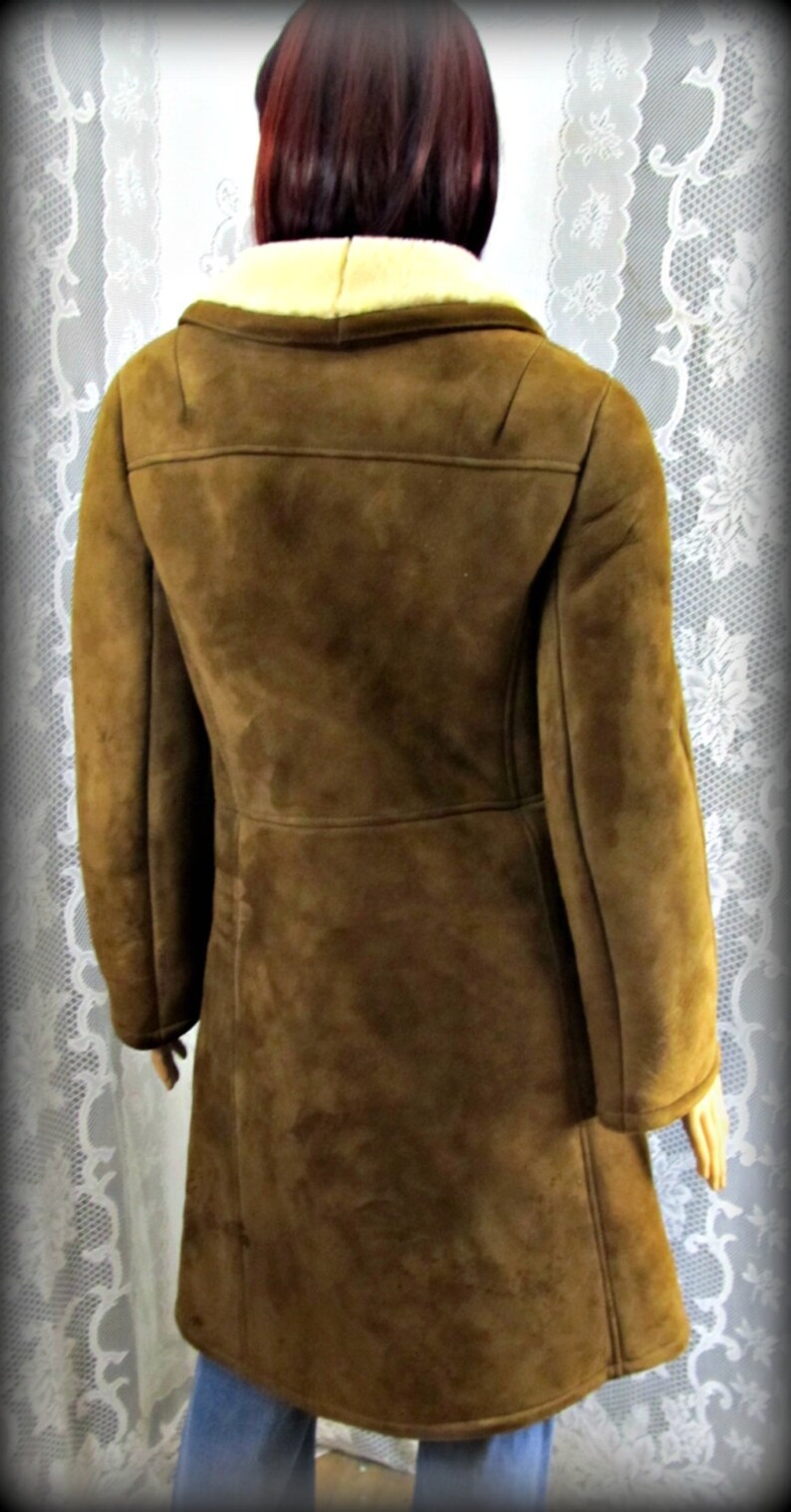 May include: A brown suede coat with a shearling collar. The coat has a long, fitted silhouette and a single-breasted closure.