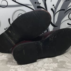 Puede incluir: Un par de zapatos de cuero burdeos con suelas de goma negra. Los zapatos est&aacute;n usados y tienen marcas de desgaste en las suelas.