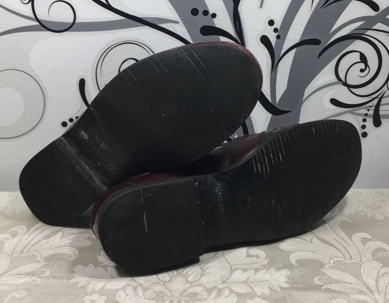 Puede incluir: Un par de zapatos de cuero burdeos con suelas de goma negra. Los zapatos est&aacute;n usados y tienen marcas de desgaste en las suelas.