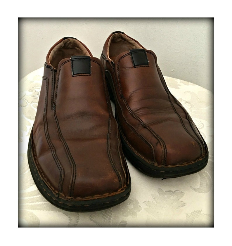 May include: A pair of brown leather slip-on shoes with black stitching and a black rubber sole.
