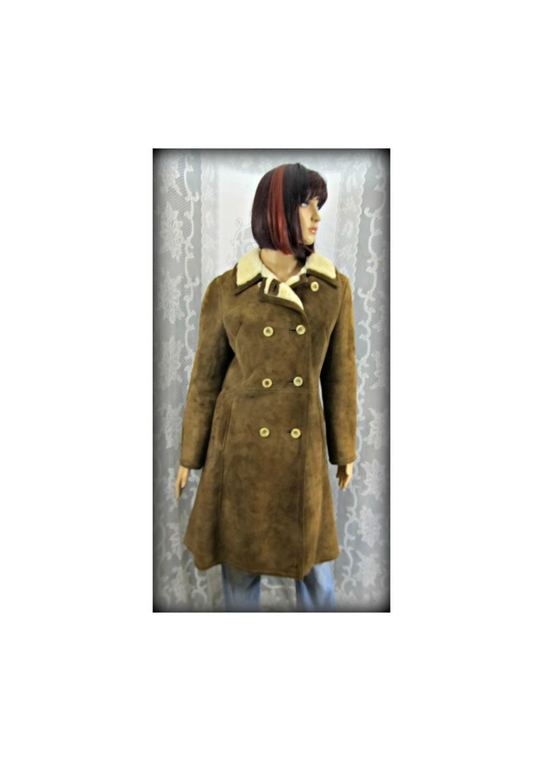 May include: A brown suede coat with a white faux fur collar and double breasted closure. The coat has a long, A-line silhouette.