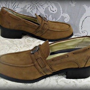 May include: A pair of brown suede loafers with a buckle detail. The loafers have a low heel and a chunky sole.