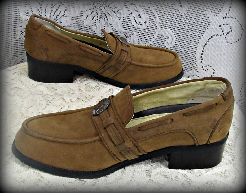 May include: A pair of brown suede loafers with a buckle detail. The loafers have a low heel and a chunky sole.