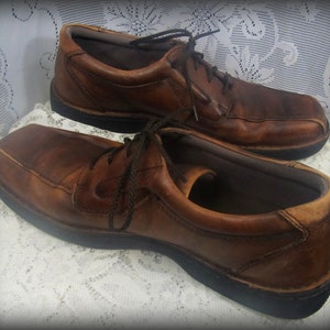 May include: A pair of brown leather lace-up shoes with a dark brown sole. The shoes are worn and have a distressed look.