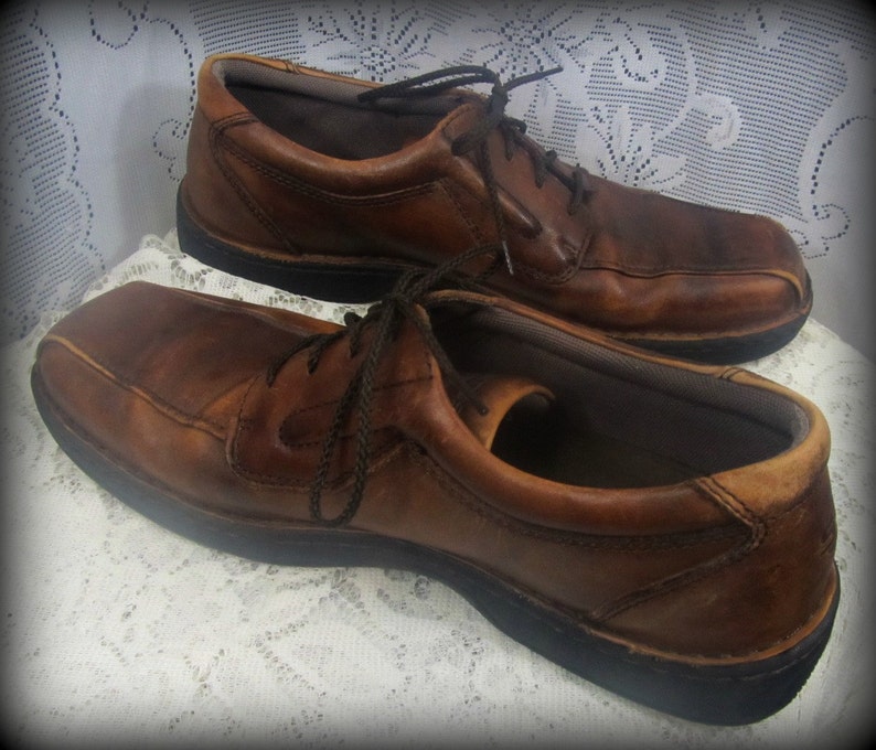 May include: A pair of brown leather lace-up shoes with a dark brown sole. The shoes are worn and have a distressed look.
