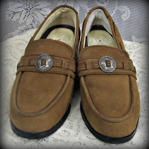 May include: A pair of brown leather loafers with silver star-shaped buckles. The loafers have a simple design and a classic look.