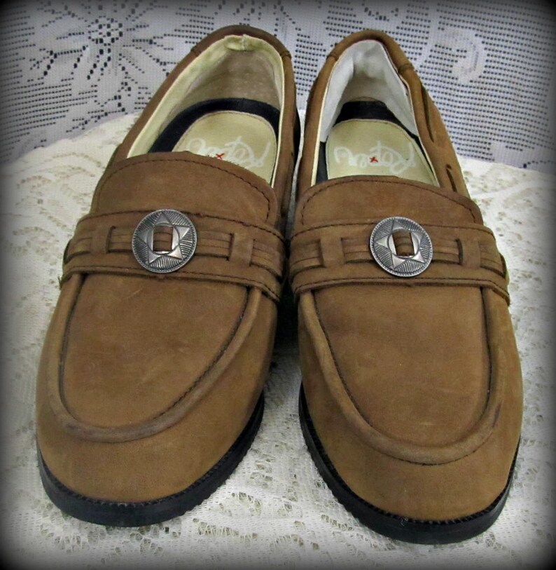 May include: A pair of brown leather loafers with silver star-shaped buckles. The loafers have a simple design and a classic look.