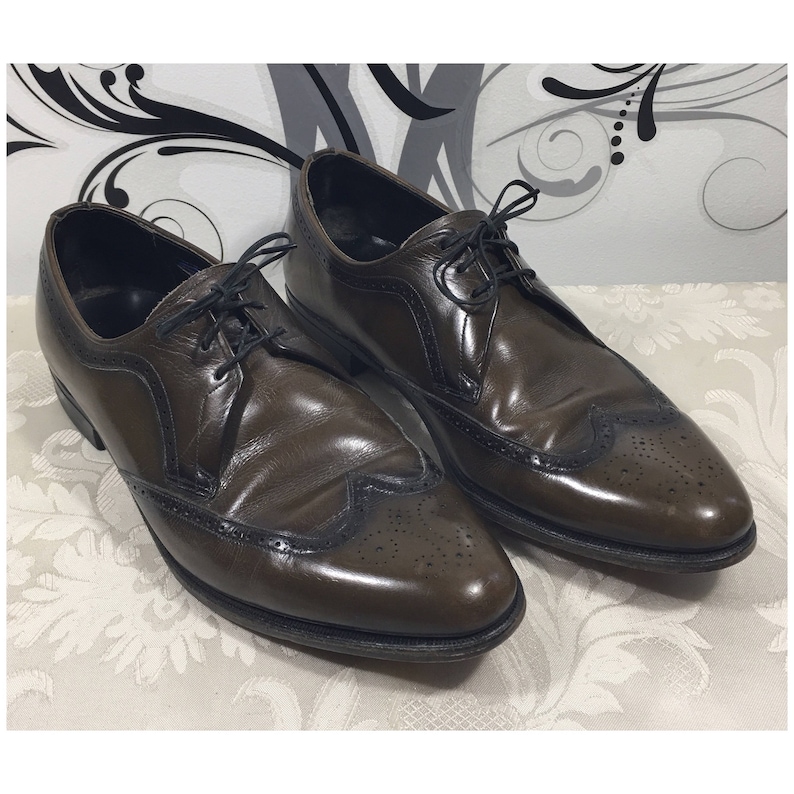 May include: A pair of brown leather lace-up shoes with wingtip detailing. The shoes have a brogue pattern and a polished finish.