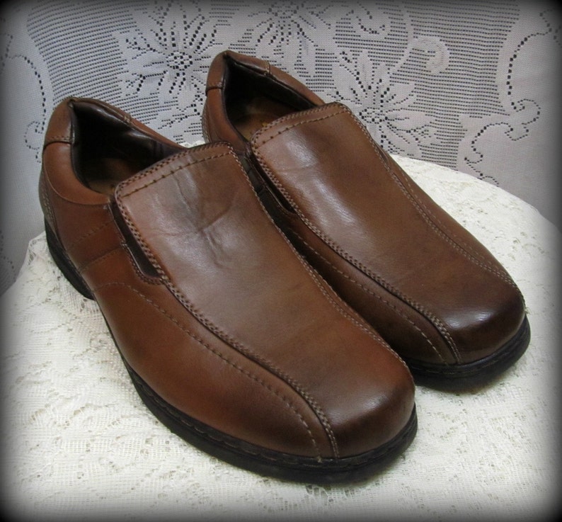 Puede incluir: Un par de zapatos de vestir marrones de cuero con un dise&ntilde;o cosido. Los zapatos tienen una punta redonda y una suela gruesa.