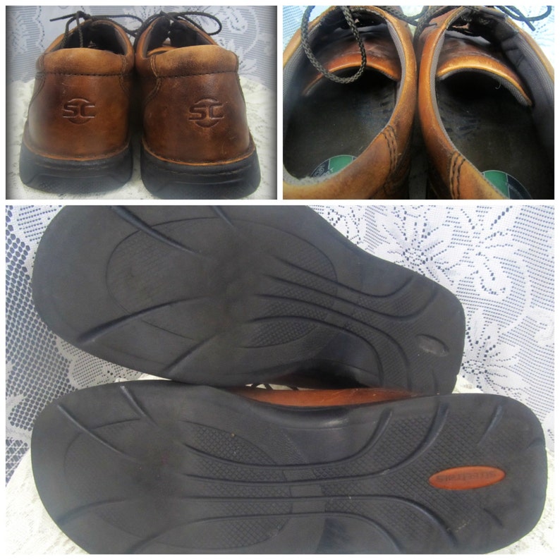 May include: A pair of brown leather shoes with black soles. The shoes have a lace-up closure and a logo on the side. The shoes are shown from the top and the bottom.