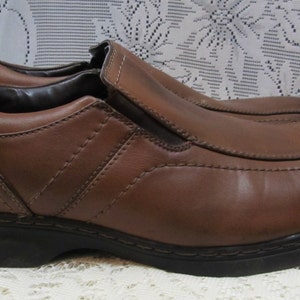 Puede incluir: Zapatos marrones de cuero con cierre de slip-on y suela de goma negra.
