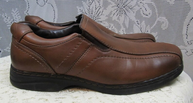 Puede incluir: Zapatos marrones de cuero con cierre de slip-on y suela de goma negra.