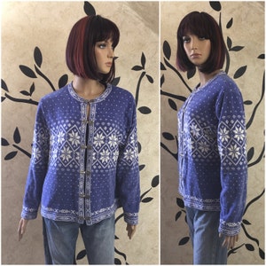 May include: A blue and white patterned cardigan with a button closure. The cardigan features a snowflake design and is made from a soft, knitted fabric.