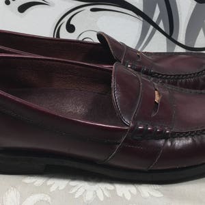Puede incluir: Un par de mocasines de cuero burdeos con un detalle de tira de penique. Los mocasines tienen un dise&ntilde;o cl&aacute;sico y est&aacute;n hechos de cuero de alta calidad.