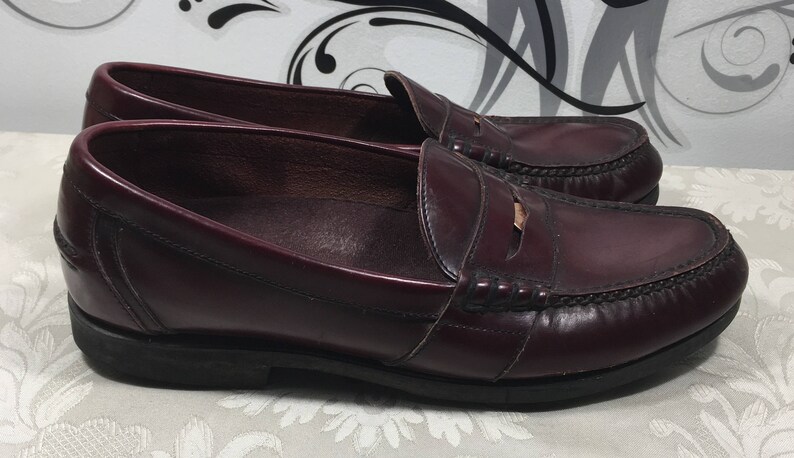 Puede incluir: Un par de mocasines de cuero burdeos con un detalle de tira de penique. Los mocasines tienen un dise&ntilde;o cl&aacute;sico y est&aacute;n hechos de cuero de alta calidad.