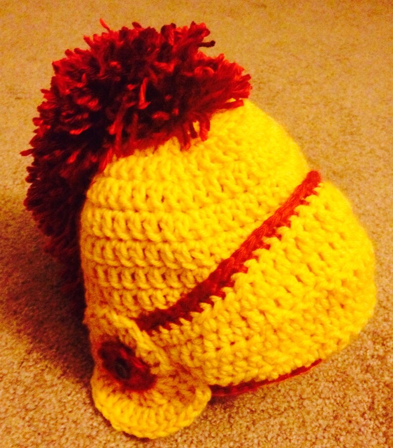 May include: A yellow crocheted hat with a red pom-pom on top and a red stripe around the brim.