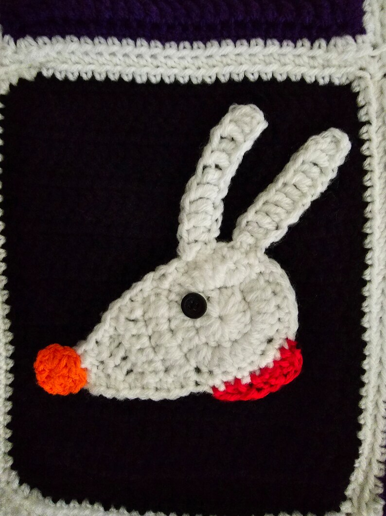 May include: White crocheted animal head with a red nose and red mouth, on a black background with a white crocheted border.