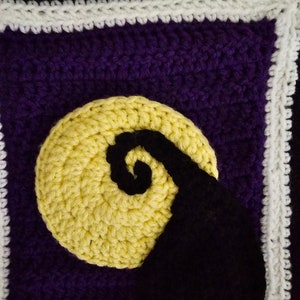 May include: A crocheted square with a purple background, a yellow crescent moon, and a black silhouette of a spiral. The square is bordered with white crochet.