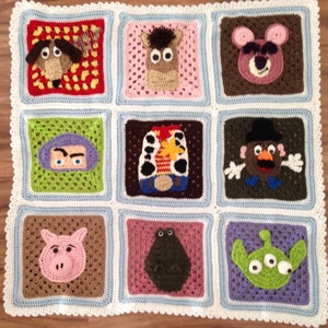 May include: A handmade crochet blanket featuring squares with characters from a popular animated film. The squares are in various colors, including red, pink, green, and brown, with white and blue borders. The blanket has a white scalloped edge.