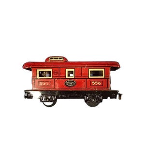 May include: A vintage red toy train caboose with black wheels and accents. The caboose features the text "250" and "556", along with "New York Central Lines" on the side. The windows have gold trim.
