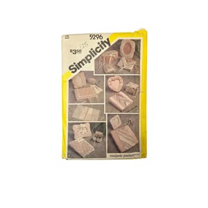 May include: A vintage Simplicity sewing pattern, number 5296, with a yellow and white design. The pattern features various craft projects, including small boxes and decorative items. The cover displays a collage of finished projects.