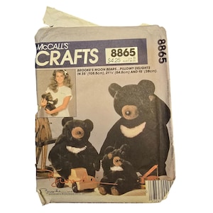 Könnte beinhalten: Eine McCall's Crafts Schnittmusterhülle 8865 für Brooke's Moon Bears, die drei schwarze Plüschbären mit weißen Brustabzeichen zeigt. Die Verpackung gibt die Größen 108,5 cm, 54,5 cm und 38 cm an und enthält ein Foto einer Person mit einem Bären.