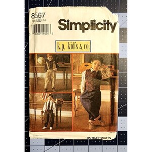 Könnte beinhalten: Simplicity Schnittmuster Nummer 8567 für Jungenbekleidung in den Größen 5-8. Das Schnittmuster enthält drei verschiedene Outfits: ein weißes Hemd mit Weste und karierter Hose, ein weißes Hemd mit Hosenträgern und Khakihose sowie ein weißes Hemd mit Krawatte und schwarzer Hose. Das Schnittmuster trägt den Titel "k.p. kid's & co."