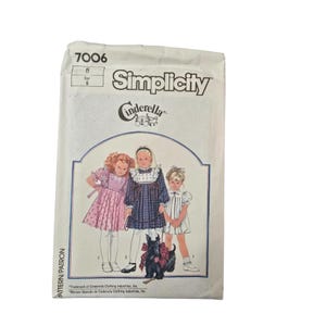 May include: A Simplicity sewing pattern envelope featuring a Cinderella design. The envelope displays illustrations of three young girls in dresses, with a black dog wearing a bow. The text includes "Simplicity" and "Cinderella".